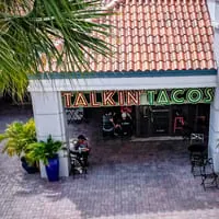 Overhead view of the Talkin' Tacos restaurant entrance with outdoor seating and palm trees.