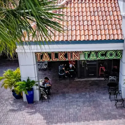 Overhead view of the Talkin' Tacos restaurant entrance with outdoor seating and palm trees.
