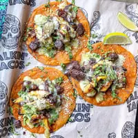 Three Talkin' Tacos with meat, cheese, cilantro, and lime wedges on branded paper.