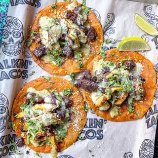 Three Talkin' Tacos with meat, cheese, cilantro, and lime wedges on branded paper.