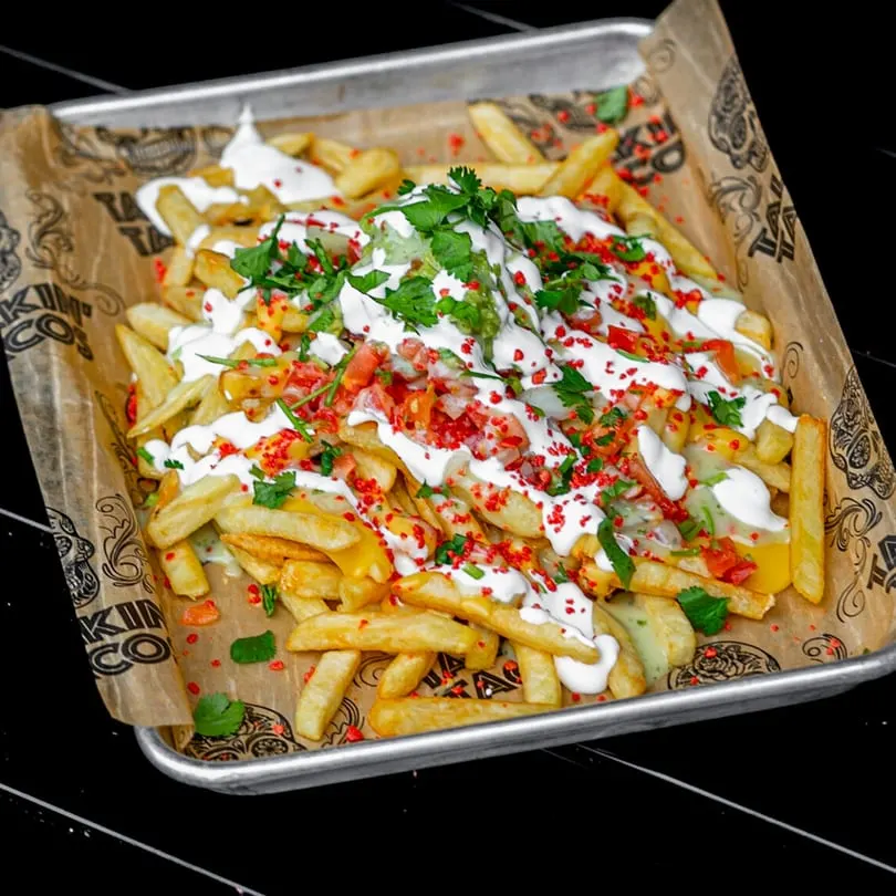 Talkin' Tacos loaded fries with white sauce, red sprinkles, guacamole, and cilantro on a tray.