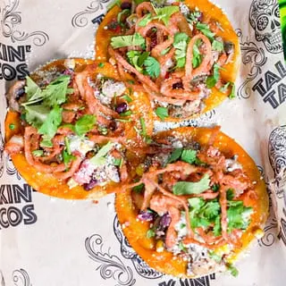 Three Talkin' Tacos with crispy onions, cilantro, and cheese on branded paper.