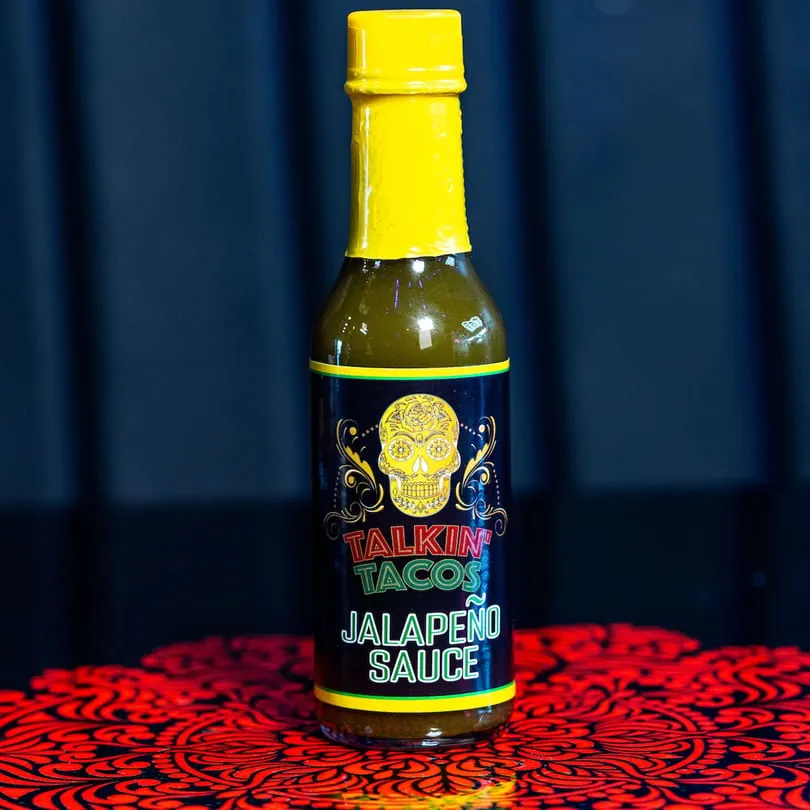 A bottle of Talkin' Tacos Jalapeño Sauce with a yellow cap and a sugar skull label.
