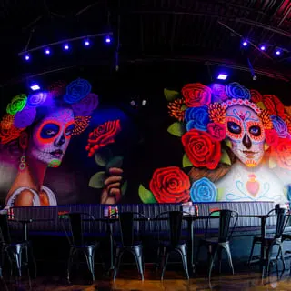 Talkin' Tacos restaurant interior with vibrant Day of the Dead murals and black booth seating.