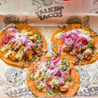 Three Talkin' Tacos with chicken, cheese, red onions, and cilantro on branded paper.