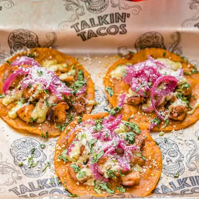 Three Talkin' Tacos with chicken, cheese, red onions, and cilantro on branded paper.