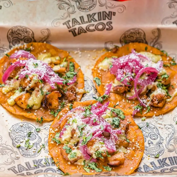 Three Talkin' Tacos with chicken, red onions, cheese, and cilantro on branded paper.