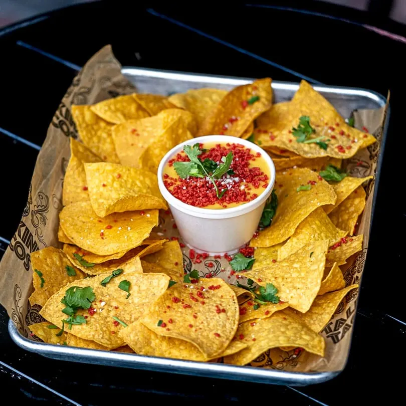 Talkin' Tacos' tray of tortilla chips with a cup of cheese dip, topped with red crumbs and cilantro.