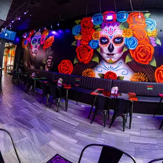 Talkin' Tacos restaurant interior with vibrant Day of the Dead murals and purple lighting.