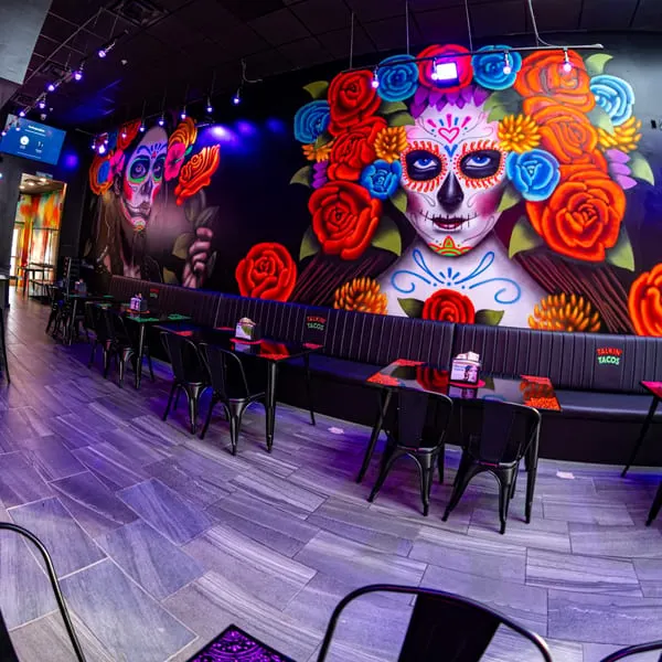 Talkin' Tacos restaurant interior with vibrant Day of the Dead murals and black tables with benches.