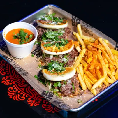 Four Talkin' Tacos birria tacos with fries and a side of consommé on a metal tray.