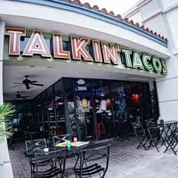 Exterior of Talkin' Tacos restaurant with outdoor seating, featuring the prominent neon sign.