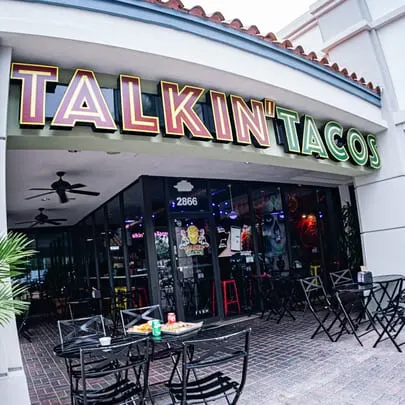 The exterior of Talkin' Tacos restaurant with outdoor seating and food on tables.