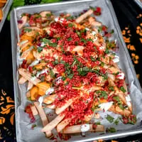 A tray of Talkin' Tacos loaded fries with cheese, red sprinkles, cilantro, and white sauce.
