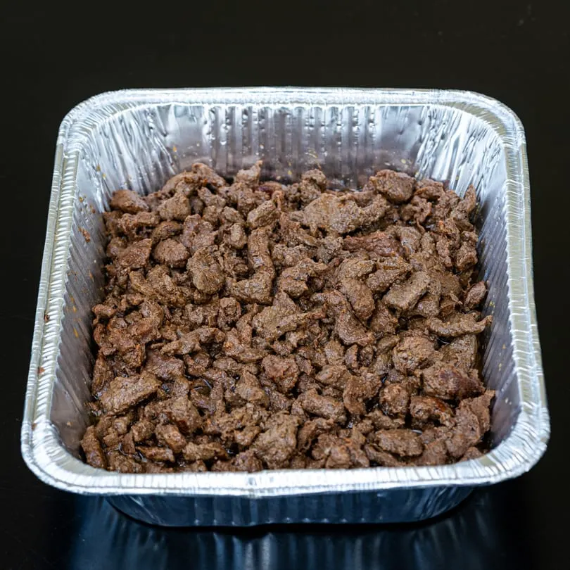 Close-up of seasoned beef chunks in a silver foil tray, ready for Talkin' Tacos.