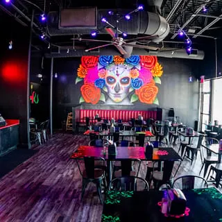Interior of Talkin' Tacos restaurant with a large colorful sugar skull mural and empty tables.