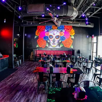 The interior of Talkin' Tacos restaurant with a large colorful sugar skull mural and dining tables.