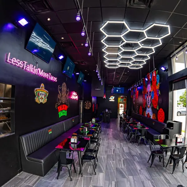 The interior of Talkin' Tacos restaurant with dark walls, neon signs, and colorful murals.