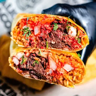 A Talkin' Tacos burrito cut in half, revealing rice, meat, and red sauce.